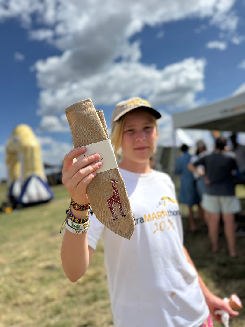 Person holding a bandana with giraffe embroidery outdoors on a sunny day