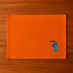 Burnt Orange Tablemat with a bird embroidery on a wooden surface