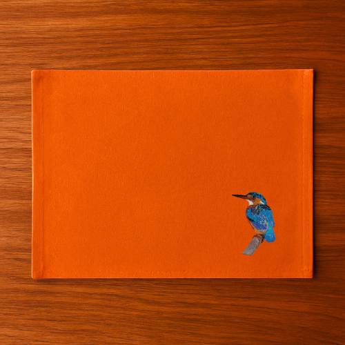 Burnt Orange Tablemat with a bird embroidery on a wooden surface