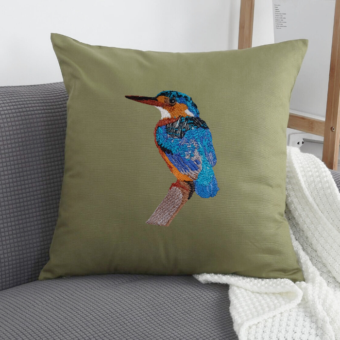 Green pillow  Cover with embroidered bird design on a gray couch.