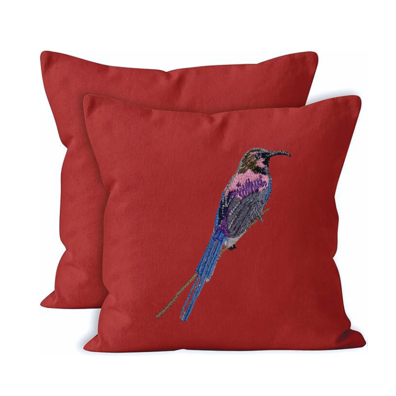 Red pillow with embroidered bird design on a white background