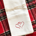 Table setting with a white napkin featuring a hearts embroidery  on a wooden table.