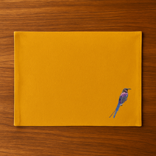 Mustard placemat with a bird embroidery on a wooden surface