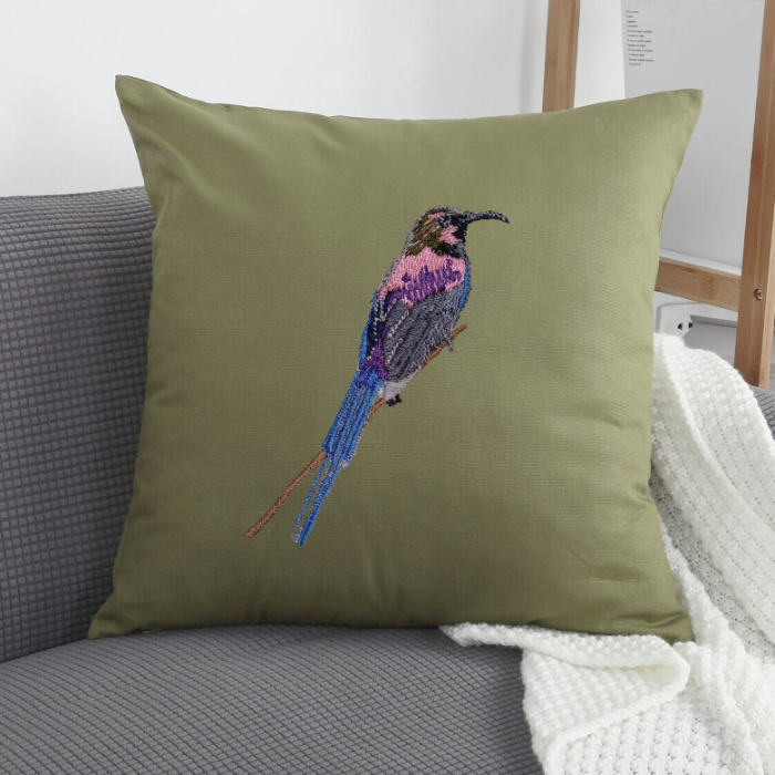 Green pillow with embroidered bird design on a gray couch.
