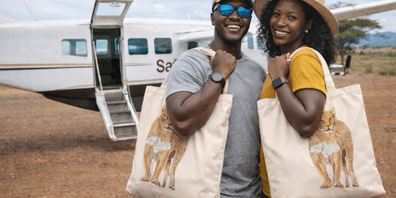 Two people holding tote bags with lion designs in front of an airplane.