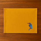 Mustard tablemat with a bird embroidery  on a wooden surface
