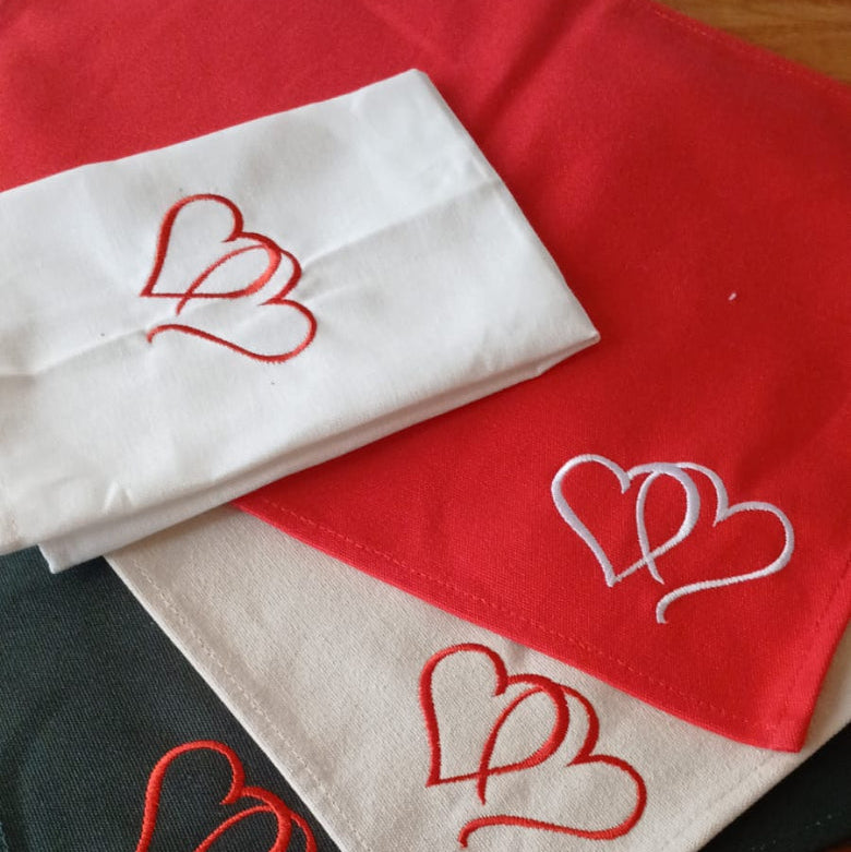 Three fabric Table Mats with embroidered heart designs on a wooden surface