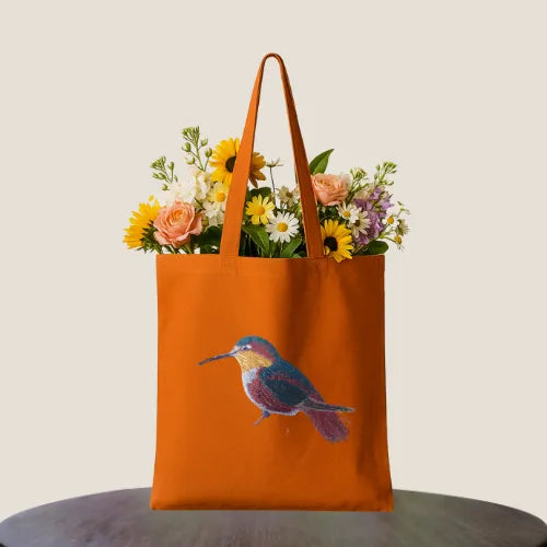 ILISAH Canvas Tote featuring a vibrant hummingbird design, available in black, burnt orange, and navy blue, perfect for ev...