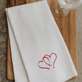 White tea towel with red heart embroidery on a wooden surface