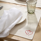 Table setting with white napkin with hearts embroidery  on a wooden table.