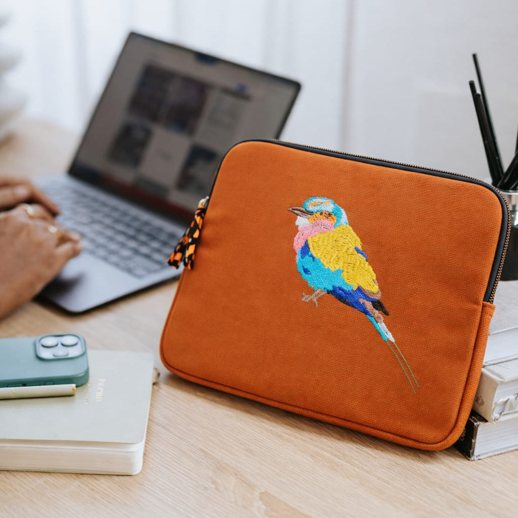 Orange laptop sleeve with a bird design on a desk with a laptop and phone.